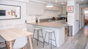 A modern kitchen with white cabinetry, a central island with stools, and a dining area with a table and chairs.