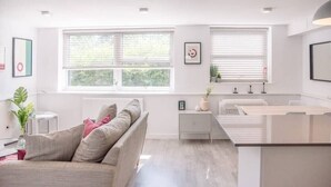 Un saló modern i ben il·luminat amb un sofà, una taula de centre i una zona de cuina amb un taulell i armaris.