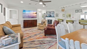 A spacious living area with a large flat-screen TV, a fireplace, and a dining table with chairs.