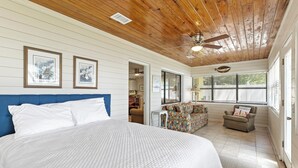 A bedroom with a large bed, a ceiling fan, and framed pictures on the wall.