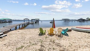 A beach with colorful Adirondack chairs, a red umbrella, and a kayak.