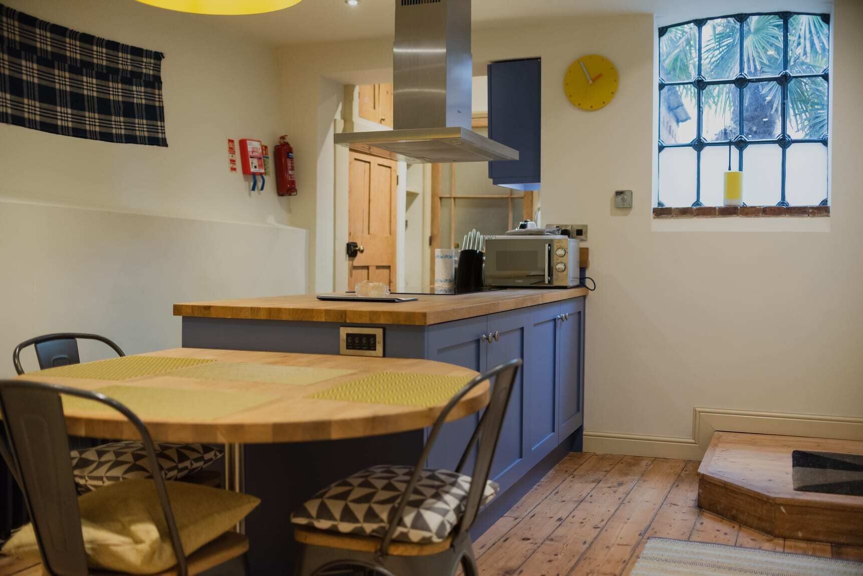 A compact kitchen with a wooden table and chairs, a microwave, and a window with a view of palm trees.