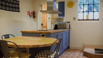 A compact kitchen with a wooden table and chairs, a microwave, and a window with a view of palm trees.