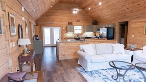 A cozy cabin interior with a wooden interior, a white sofa, a dining table, and a kitchen area.
