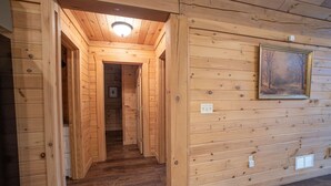 A wooden interior with a hallway leading to a room, a ceiling light, and a framed picture on the wall.