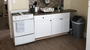 A kitchen with white cabinets, a gas stove, a microwave, and a trash can.