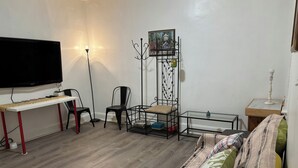 A living room with a flat-screen TV, a sofa, a coffee table, a chair, a small table, and a decorative plant.