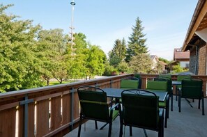 An outdoor patio with green metal chairs and tables, surrounded by trees and a wooden fence.