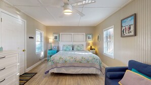 Ein Schlafzimmer mit einem Bett, einer Kommode, einem blauen Sessel und einem Deckenventilator.