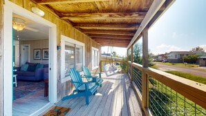 Eine Holzterrasse mit Schaukelstuhl und Sofa, eine überdachte Veranda und Blick auf die Straße.