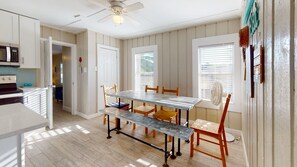 A dining area with a table and chairs, a ceiling fan, and a view of the outside through a window.