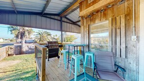 A covered outdoor area with a grill, two bar stools, and a cushioned bench.