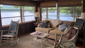 Une pièce confortable donnant sur un lac, avec un fauteuil à bascule, un canapé avec des coussins et une petite table sur laquelle sont posés des magazines.
