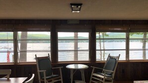 Une pièce avec vue sur un lac, deux fauteuils à bascule, une petite table ronde et un mur en bois.