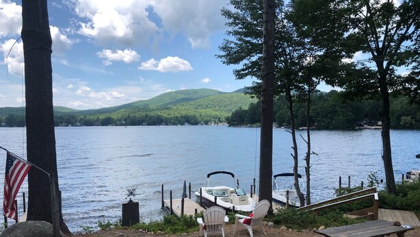 Une terrasse au bord du lac, avec des fauteuils Adirondack, une table de pique-nique et un bateau amarré au loin.