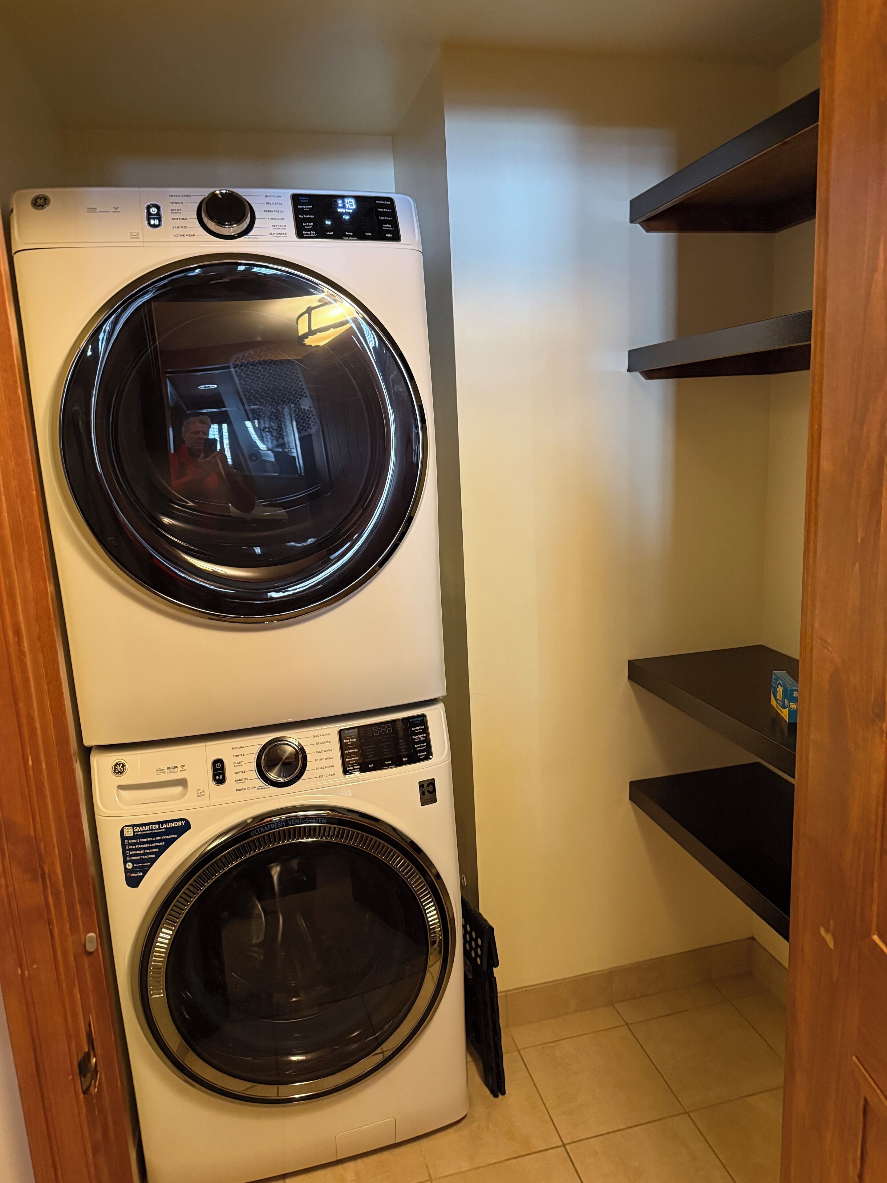 A stacked washer and dryer unit in a laundry room with a wooden door and tiled floor.