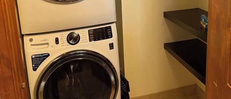 A stacked washer and dryer unit in a laundry room with a wooden door and tiled floor.