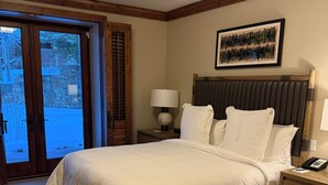 Una habitación de hotel con una cama grande, cabecera de madera, mesita de noche con lámpara y un cuadro enmarcado en la pared.