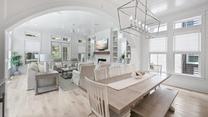 Ein geräumiges Wohnzimmer mit hoher Decke, großen Fenstern und einem Essbereich mit Holztisch und Stühlen.