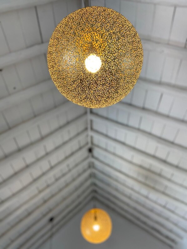 A spherical chandelier with a textured surface hanging from a ceiling with a grid pattern.
