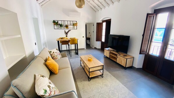 A living room with a sofa, coffee table, TV stand, and a dining area with chairs and a table.
