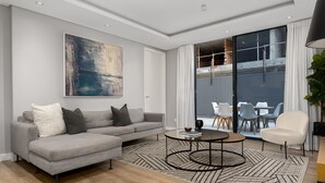 A modern living room with a grey sofa, a coffee table, and a large abstract painting on the wall. - Chic Green Point Apartment | Fast WiFi | BBQ Patio (Cape Town)