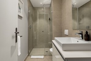 Et moderne badeværelse med et glasafskærmet brusebad, en hvid vask og et stort spejl.