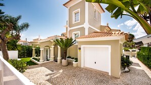 A two-story building with a tiled roof, a paved driveway, and a white garage door. - Rosal 27 (Albufeira)