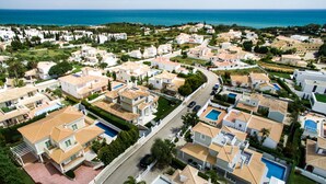 An aerial view of a coastal residential area with houses, swimming pools, and a clear view of the sea. - Rosal 27 (Albufeira)