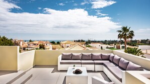 A rooftop terrace with a large sectional sofa, a small table, and a view of the cityscape and ocean. - Rosal 27 (Albufeira)