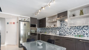 Uma cozinha moderna com mesa de jantar de vidro, geladeira de aço inoxidável, armários escuros e backsplash com azulejos azuis.