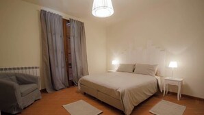 A bedroom with a bed, two bedside tables with lamps, a grey sofa, and a window with curtains.