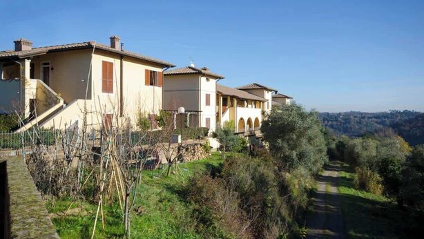 A row of traditional Mediterranean-style villas with terracotta roofs, a stone pathway, and a view of the surrounding hills.