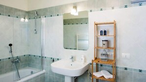 A bathroom with a bathtub, a sink, and a wooden shelf with toiletries.