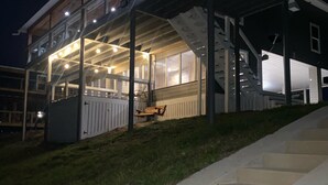 Et moderne hus med et overdækket udendørsareal, en trappe op til indgangen og et veloplyst interiør.