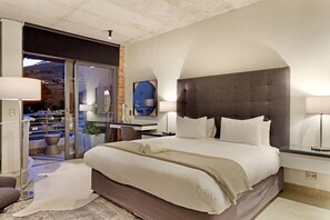 Une chambre d’hôtel moderne avec un grand lit, une porte vitrée donnant sur un balcon et une vue sur la ville.
