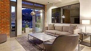 Ein modernes Wohnzimmer mit Sofa, Couchtisch und Lampe. Ein großes Fenster bietet Blick auf eine Stadtlandschaft und Berge.