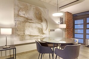 Une salle de réunion moderne, dotée d’une table en verre, de quatre chaises, d’un grand tableau abstrait au mur et d’un mur décoratif en briques.