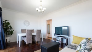 Ein modernes Wohnzimmer mit Essbereich, Fernseher und einer großen Pflanze.