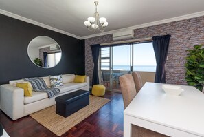 A modern living room with a sofa, ottoman, and a dining table.