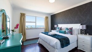 Ein Schlafzimmer mit einem großen Bett, einem Nachttisch, einer Kommode, einem Spiegel und einem Fenster mit Vorhängen.