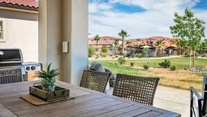 Un patio al aire libre con una parrilla, sillas de mimbre y vistas a un barrio residencial con casas y jardines.