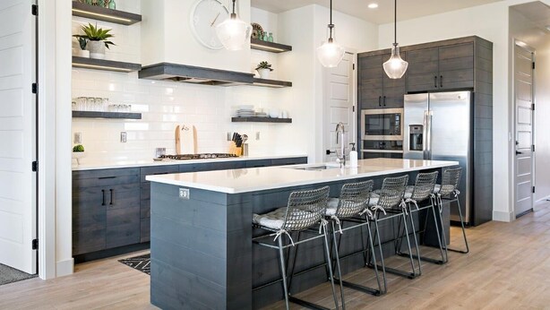 Una cocina moderna con una isla central, taburetes de bar, electrodomésticos integrados e iluminación colgante.