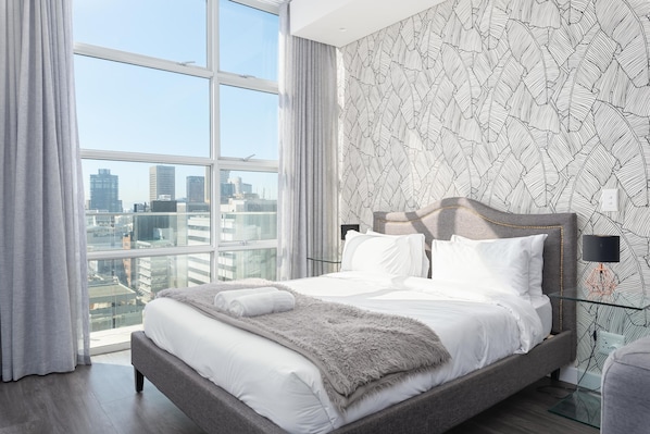 Une chambre d’hôtel moderne avec un grand lit, une vue sur la ville et un papier peint à motifs.