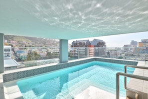 Une piscine à débordement située sur le toit, offrant une vue dégagée sur le paysage urbain et les collines en arrière-plan.