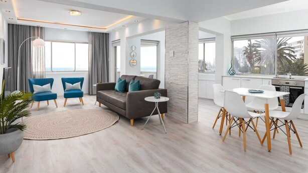 A modern living room with a grey sofa, blue armchairs, a round coffee table, and a dining area with white chairs and a white table. - Beachfront Gem with Amazing Views! (Cape Town)