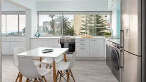 A modern kitchen with a dining area, large windows, and a view of palm trees and buildings. - Beachfront Gem with Amazing Views! (Cape Town)