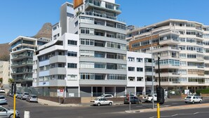 A multi-story residential building with balconies, a parking area, and a clear view of a mountain in the background. - Beachfront Gem with Amazing Views! (Cape Town)