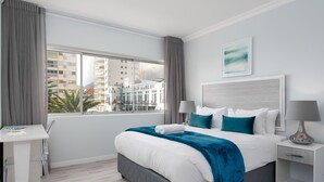 A modern hotel room with a large bed, a desk, and a view of the cityscape. - Beachfront Gem with Amazing Views! (Cape Town)