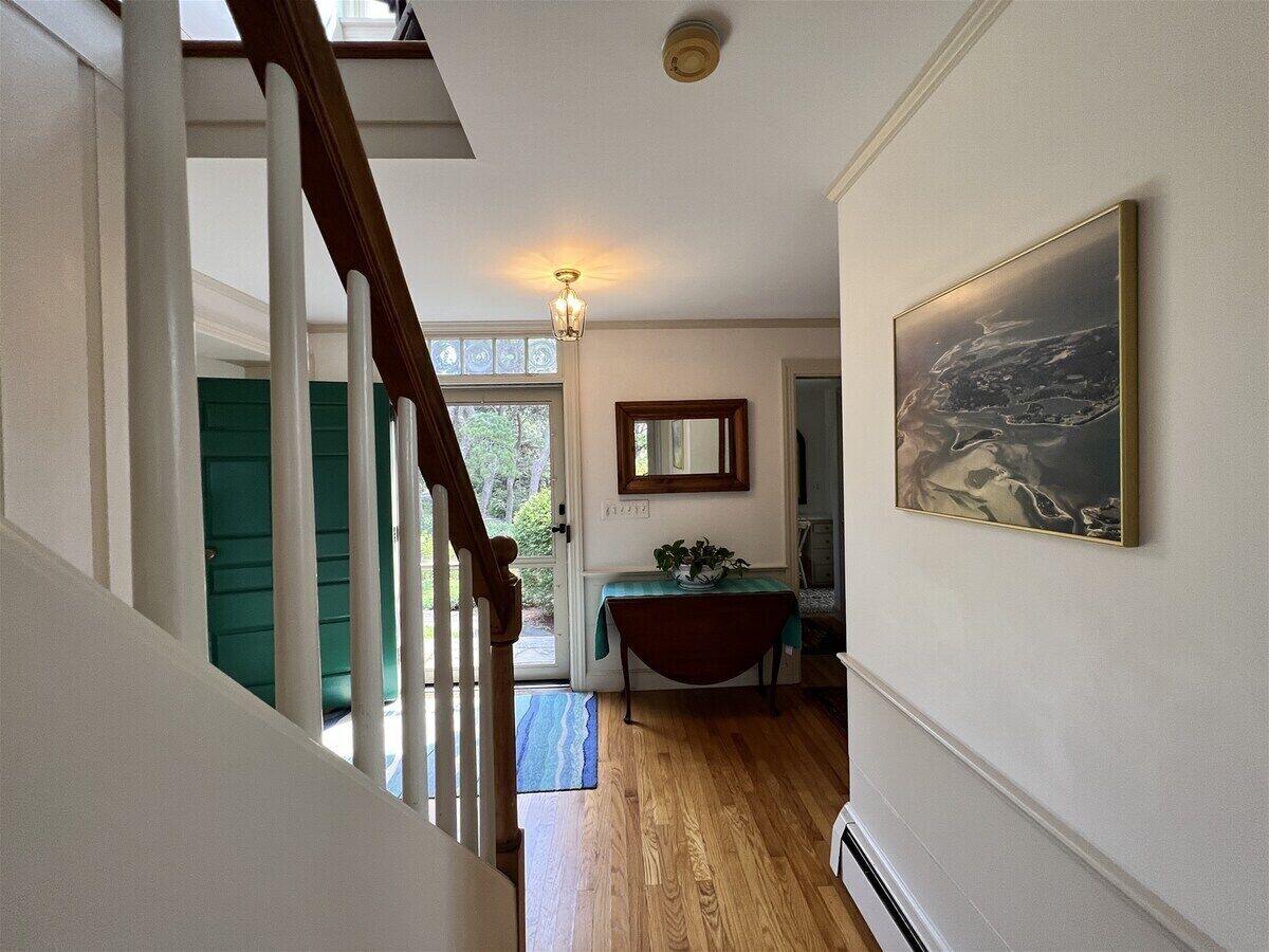 A staircase leading to a room with a wooden floor, a green door, a table with a plant, and a framed picture on the wall.